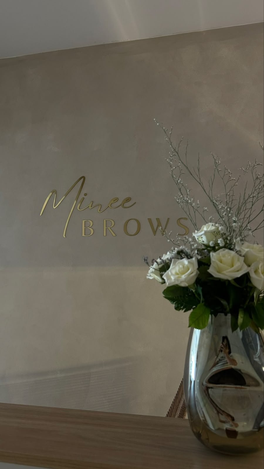 Detalle del estudio Mine Brow Studio con flores blancas y su insignia dorada
